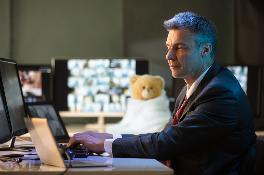 Man working at a computer with a teddy bear in a blanket next to him
