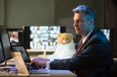 Man working at a computer with a teddy bear in a blanket next to him